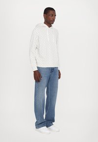 Vit huvtröja med ett geometriskt mönster, i kombination med ljusblå raka jeans och vita sneakers. Enkel design, avslappnad passform.