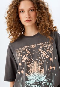 Camiseta de algodón negra con un diseño gráfico en tonos pastel de una mujer con una mariposa, rodeada de motivos florales y celestiales.