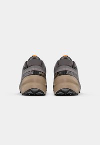 Salomon Speedcross 6 Schuhe, graues Textiloberteil, schwarze und beige Sohle, orangefarbene Akzent am Fersenbereich, ausgeprägtes Profilmuster der Außensohle.