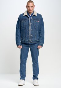 Denim jacket koos lambanahast kraega, helesinine pesu, kaks rinna taskut ja nööbid ees, paaritatud vastava värvi teksade ja valgete tennisekingadega.