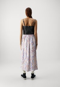 Svart smocket crop top med tynne stropper, kombinert med et langt, pastellfarget paisley-mønstrete skjørt. Modellen har på seg svarte joggesko.
