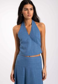 Top halter azul con tejido texturizado, diseño envolvente y longitud corta. Presenta un escote en forma de V y material suave y ligero.