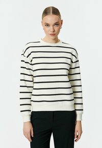 Krämsweater med svarta horisontella ränder, rund halsringning och långa ärmar. Tyget verkar mjukt med ribbade cuffs och nederkant.