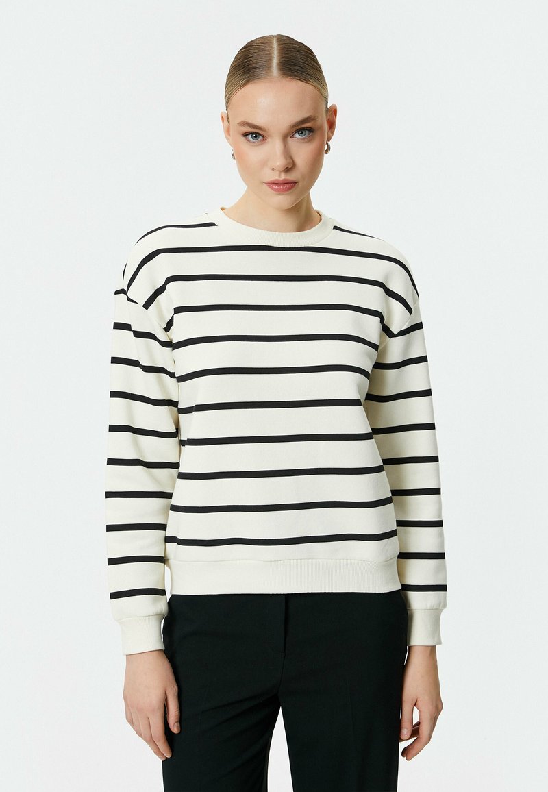 Krämsweater med svarta horisontella ränder, rund halsringning och långa ärmar. Tyget verkar mjukt med ribbade cuffs och nederkant.