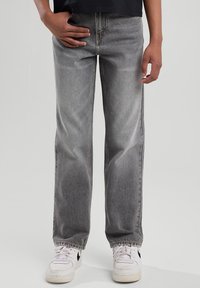 Jeans de denim gris con corte recto, lavado desvaído, diseño de cinco bolsillos y costuras sutiles. Combinados con zapatillas blancas.