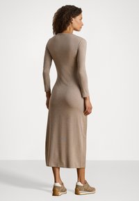Pitkä beige mekko, jossa on vartalonmyötäinen siluetti ja pitkät hihat. Sujuva, joustava kangas ja ribbitetty pinta. Yhdistetty beigen väristen lenkkareiden kanssa.