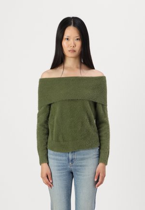 Olive green off-the-shoulder sweater in soft, textured fabric with long sleeves and a relaxed fit. Paired with light blue jeans.
