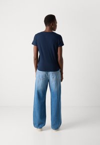 Mørkeblå tettsittende t-skjorte med korte ermer og rund hals, sammen med vide lyseblå denimbukser med baklommer.
