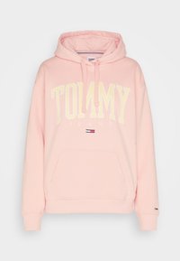 Sudadera con capucha rosa, hecha de material suave. Presenta el texto "TOMMY JEANS" en blanco, bolsillo frontal tipo canguro y un logo de la marca en la manga.