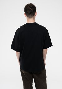 Black oversized t-shirt made of cotton, featuring a round neck and short sleeves. The back view shows a smooth texture and relaxed fit.