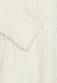 Maglione bianco a treccia, realizzato in morbido filato; presenta un colletto a coste e una trama con motivi in rilievo, creando un aspetto accogliente.
