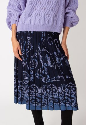 Maglione lavorato a maglia lilla con un motivo a diamante testurizzato, abbinato a una gonna plissettata blu navy con un design floreale azzurro.