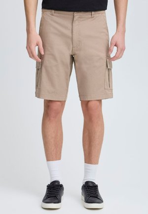 Beige cargo shorts made of cotton, featuring side pockets, a relaxed fit, and a straight hem. Worn with black shoes and white socks.