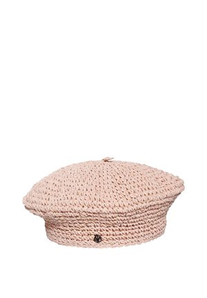 Béret crocheté rose clair avec un petit emblème décoratif rond noir sur le côté, présenté sur un fond blanc.