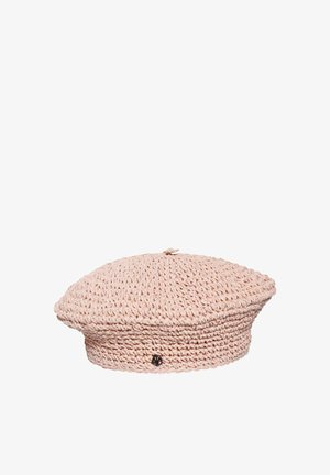 Boina de ganchillo de color rosa claro con un pequeño emblema decorativo redondo negro en el lateral, presentada sobre un fondo blanco.