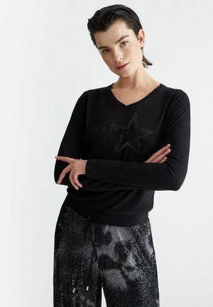 Top nero a maniche lunghe con scollo a V, caratterizzato da un design a stella in paillettes. Abbinato a pantaloni neri lucidi in paillettes con vita regolabile tramite cordoncino.
