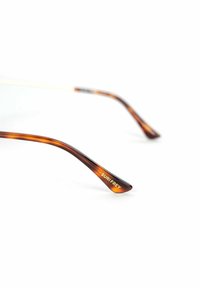 Sluneční brýle s želvovinovým vzorem a štíhlými, zakřivenými acetátovými rameny v barvách jantaru a hnědé. "SURI FREY" vytištěno zlatou barvou na vnější straně levého ramene.