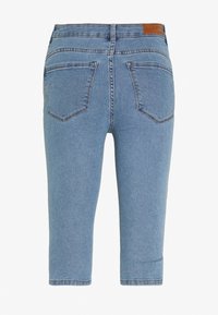 Ljusblå denim capri-jeans med medelhög midja, femficksdesign och en tan färgad läderetikett på baksidan av midjebandet.