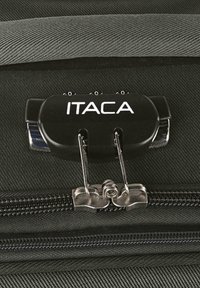 Cierre de cremallera negro con el logo "ITACA", asegurando una maleta de tela negra texturizada, con herrajes plateados y broches dobles de sujeción.