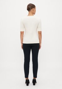 Rövid ujjú krémszínű top, négyzet alakú nyakkivágással, sötét slim-fit nadrággal és fekete magassarkú cipővel párosítva. Sima anyag, minimalista design.