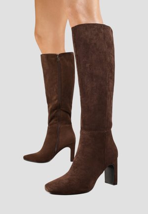 Bottes en suede marron, montantes jusqu'au genou, avec un bout pointu et un talon bloc, présentant une fermeture éclair latérale pour un enfilage facile et une texture lisse.