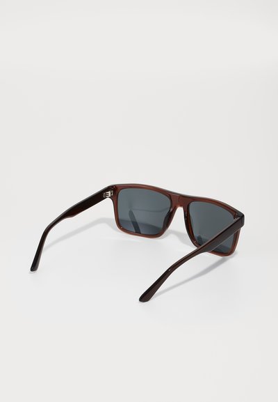 Ochelari de soare din plastic maro, cu rame pătrate, lentile gri închis și brațe subțiri. Caracteristicile de design notabile includ un model subtil pe brațe.