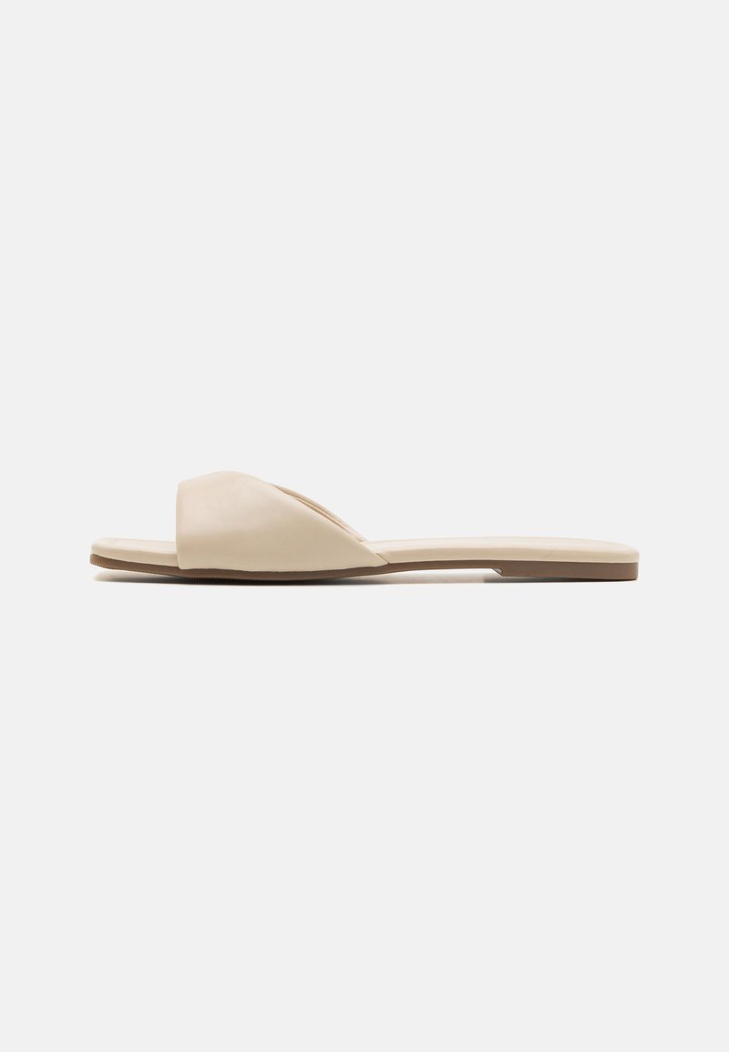 Lameed jalatsid pehmes beežis materjalis, avatud toe disainiga, sileda tekstuuriga ja minimalistliku kujuga, millel on heledat pruuni tooni talla.