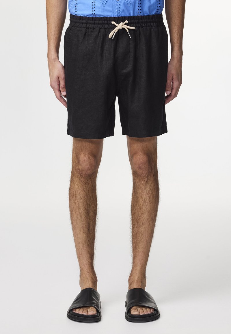 Pantaloni corti neri in lino con elastico in vita, lacci e una vestibilità comoda. Abbinati a sandali neri a scivolo.