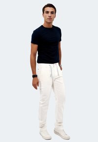 Marineblaues T-Shirt mit kurzen Ärmeln, kombiniert mit weißen Hosen und weißen Sneakers. Die Hosen verfügen über einen Kordelzug und schwarze Akzente.