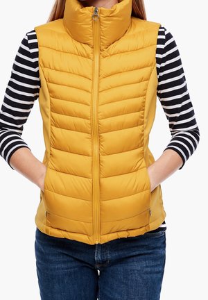 Gilet giallo imbottito con colletto alto, caratterizzato da un design trapuntato e chiusura con zip. Indossato sopra una maglietta a maniche lunghe a righe bianche e nere.