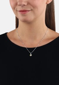 Srebrna naszyjnik z wisiorkiem w kształcie łzy z żółtym akcentem, zawieszony na cienkim łańcuszku na czarnej bluzce. Gładka faktura i minimalistyczny design.