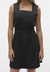 Robe noire sans manches avec des rayures verticales blanches, décolleté carré et taille cintrée, présentant une ceinture assortie avec deux boutons.