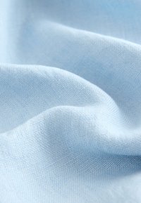 Lichtblauwe stof met een zachte, licht gestructureerde weving. Het materiaal oogt glad met een subtiele glans en hangt zachtjes in plooien.