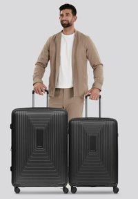 Twee zwarte hard-shell koffers met een lineair geribbeld ontwerp, voorzien van uitschuifbare handvatten en spinnerwielen, zij aan zij tentoongesteld.