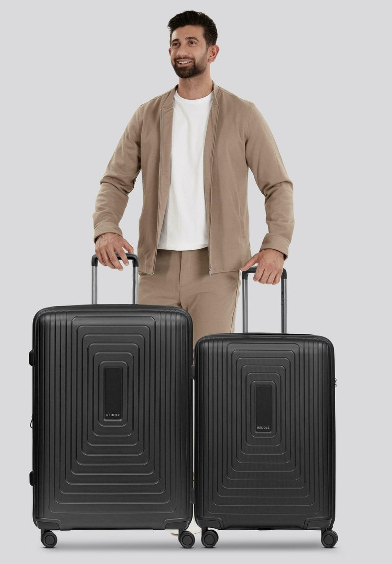 Twee zwarte hard-shell koffers met een lineair geribbeld ontwerp, voorzien van uitschuifbare handvatten en spinnerwielen, zij aan zij tentoongesteld.