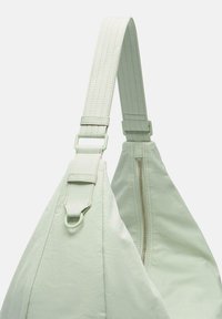 Hellgrüne Schultertasche in dreieckiger Form. Verfügt über einen breiten Riemen, einen Reißverschluss und tonale Nähte für einen strukturierten Look.