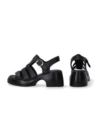 Black heeled sandals featuring multiple leather straps, a rounded toe, an ankle strap with a buckle, and a chunky, textured heel.