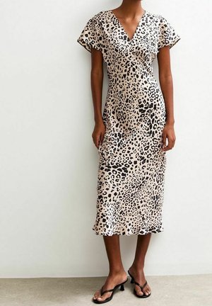 Sukienka midi w panterkę z dekoltem w kształcie litery V, krótkimi rękawami, lejącym się materiałem i lekko rozkloszowanym dołem; noszona z czarnymi klapkami.