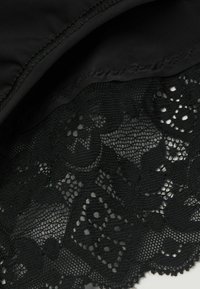 Svart tyg med intrikata spetsdetaljer, som har blommönster och vågiga kanter, kombinerat med slätt stretcht material.