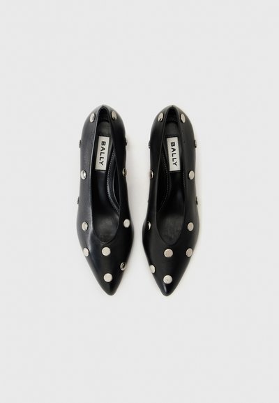 Črne usnjene čevlje s koničastimi prstnimi deli, ki imajo velike srebrne žeblje in gladko teksturo. Vidna notranja blagovna znamka. Klasična zasnova z modernimi akcenti.