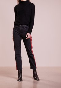 Czarny, puszysty sweter z golfem w połączeniu z ciemnoniebieskimi dżinsami z czerwonymi paskami po bokach, zestawiony z eleganckimi czarnymi botkami na obcasie.