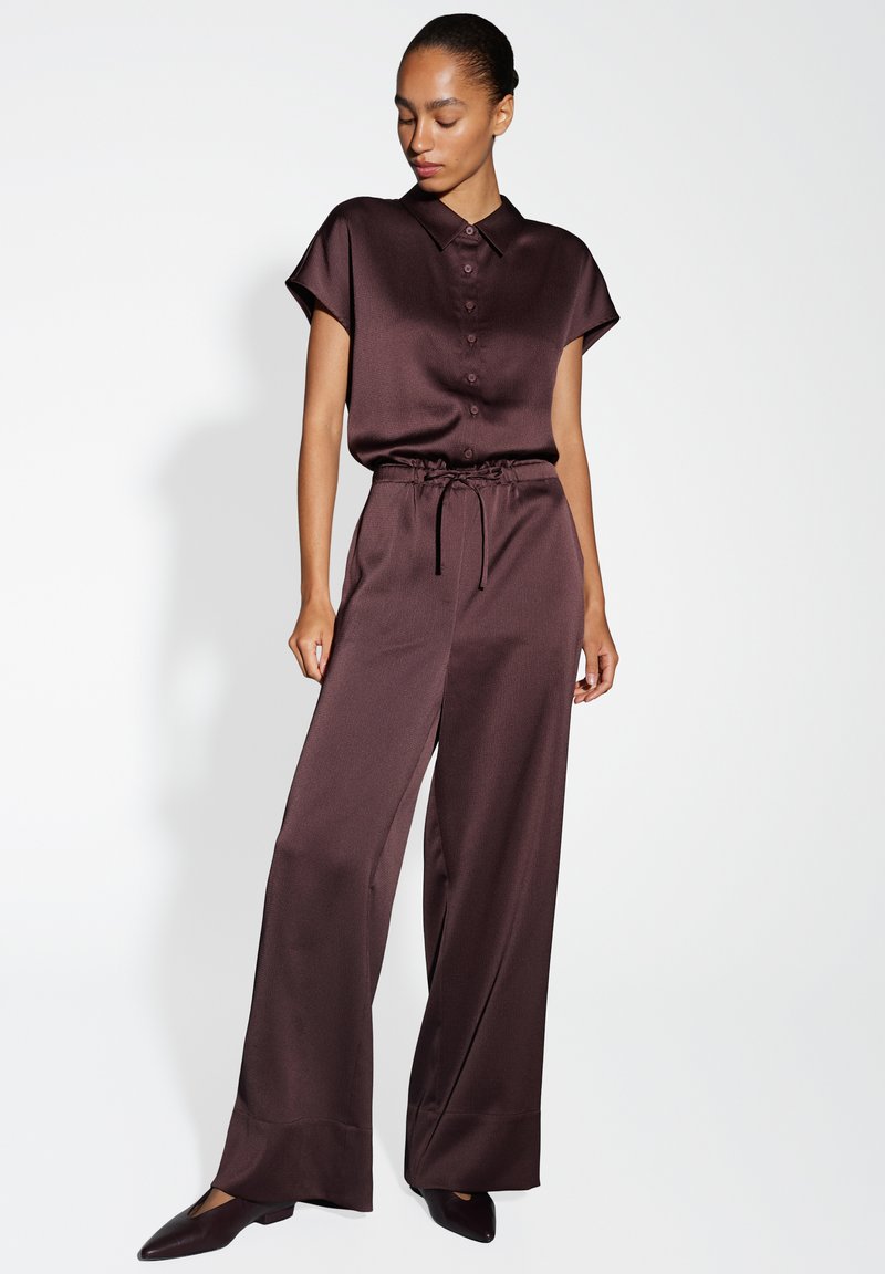 Chemise en satin marron à manches courtes avec fermeture à boutons, associée à un pantalon large taille haute. Texture lisse et design élégant mettant en valeur la coupe.