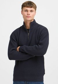 Navy Blau gestrickter Pullover mit hohem Kragen und halbem Reißverschluss. Strukturiertes Material und gerippte Bündchen runden das Design ab.
