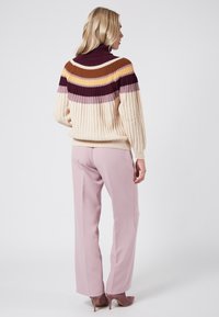 Överdimensionerad krämfärgad ribbad tröja med flerfärgade randiga axlar i lila, orange och gult, som kombineras med ljusrosa smala byxor och klackskor.