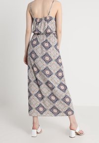 Maxi šaty s tenkými ramínky, elastickým pasem a květinovým geometrickým vzorem v námořnické modré, korálové a krémové. Bílé sandály na blokovém podpatku.