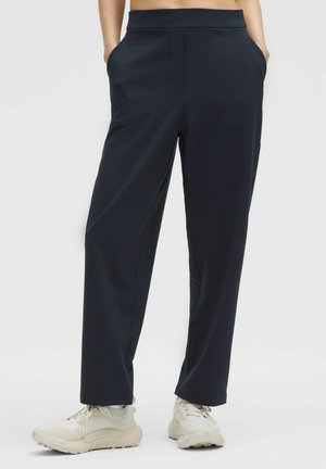 Højtaljede, navy atletiske bukser med en glat tekstur, side lommer og et lige ben-design. Båret med lyse sneakers.