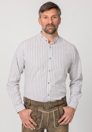 Langärmliges gestreiftes Hemd in Beige und Weiß mit Stehkragen und braunen Knöpfen. Dazu werden traditionelle braune Lederhosen mit Blumenstickerei getragen.