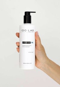 White cylindrical bottle with a black pump lid. Label reads "IDO·LAB β-GLUC+Ur 10%". Contains 400 ml of nourishing body balm. All skin types.