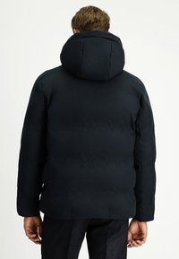 Czarna kurtka typu puffer z dużym, przypiętym kapturem, pikowanym wzorem i gładkim wykończeniem materiału. Posiada boczne kieszenie oraz dopasowany krój.