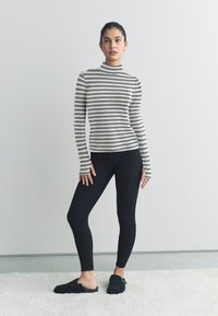 Črno-bela ovratna majica z vzorcem črt, oprijete črne pajkice in črna čevlja brez zavezovanja z zaponko, na svetli podlagi.